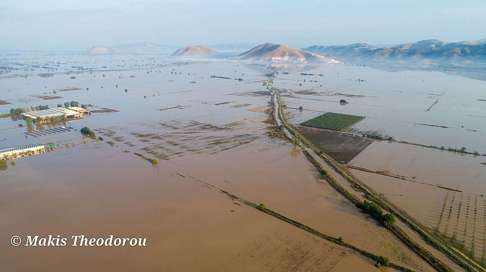Floodwater covering agricultural fields near Palamas, Thessaly, with trees and hills visible.